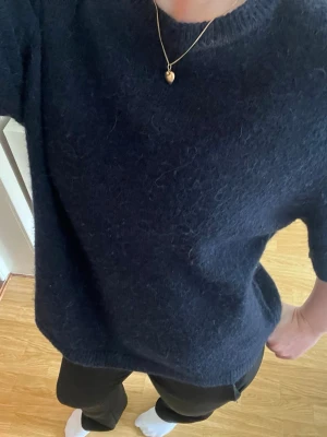 Mörkblå stickad tröja med kort ärm - Säljer en mörkblå stickad tröja med korta ärmar och rund hals. Tröjan har en mjuk, lite luddig yta och en avslappnad passform. Perfekt att styla med jeans eller kjol för en chill look.