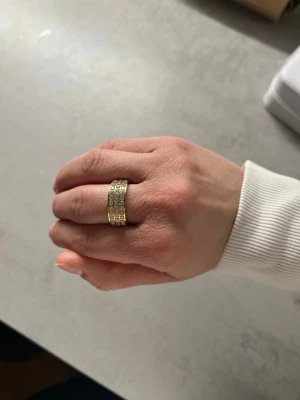 Guldfärgad ring med stenar - Snygg ring i guldfärg med tre rader glittrande stenar runt hela ringen. Ringen har en modern och lyxig känsla. Stainless steel med tjock plätering. Säljer i flera storlekar: 6, 7, 8