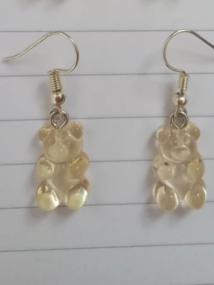 Ljusgula björn örhängen  - Säljer ett par unika örhängen med ljusgula gummibjörns-hängen i plast. Örhängena har krokar i metall och är knappt använda. 
