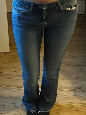 Mörkblå bootcut jeans - Säljer ett par mörkblå bootcut jeans med klassisk femficksdesign och låg midja. Jeansen har lätt slitna detaljer vid benslut. Från only storlek 34