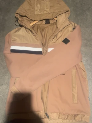 Beige Hugo Boss vindjacka (limeted edition) - Säljer en använd men väldigt fin jacka från Hugo Boss. Limited Edition i storlek S. Välskött och i bra skick.  100% äkta. Hör av dig vid intresse.