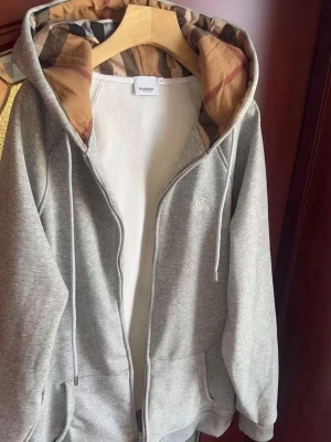 Grå zip hoodie från Burberry - Snygg grå zip hoodie från Burberry med klassiskt rutigt foder i huvan och vita dragsnören. Hoodien har fickor framtill och en liten diskret Burberry-logga på bröstet. Tillverkad i mjukt bomullsmaterial för maximal komfort.