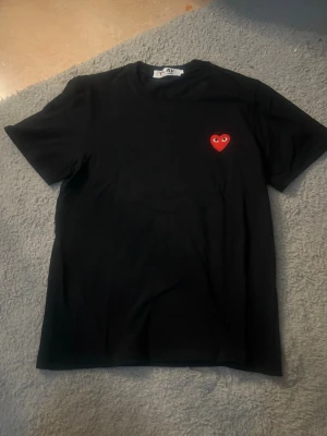 Svart Comme des Garçons Play t-shirt - Cool svart t-shirt från Comme des Garçons Play med det ikoniska röda hjärtat med ögon på bröstet. T-shirten är i storlek S och är endast använd ett fåtal gånger.