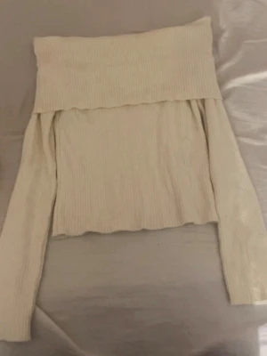 Offshoulder ribbad topp från H&M - Trendig offshoulder topp från H&M i ribbad, ljusbeige bomullsmix. Toppen har långa ärmar och en bred kant upptill som ger en snygg och modern look. Perfekt att styla med jeans eller kjol för en cool vibe.