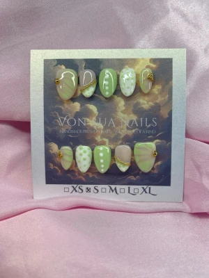 MatchaPop (S);Short Almond - Handgjorda press-on naglar u grönt med vita prickar, halvfrench och guldfärgade kedjedetaljer. S: 15 mm, 11,5 mm, 12 mm, 11 mm, 9 mm . Perfekt för dig som vill ha unika och trendiga naglar. 