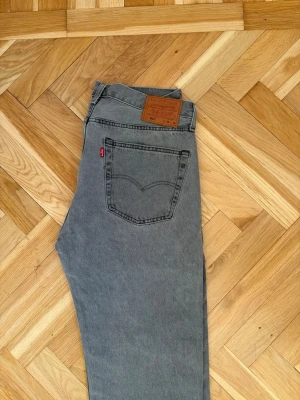 Grå Levi's 501 jeans raka ben - Säljer ett par klassiska grå Levi's 501 jeans med raka ben och hög midja. Jeansen har fem fickor, knappgylf och den ikoniska läderlappen bak i midjan. Tillverkade i slitstark bomull med vintage vibe och snygg tvättad look.