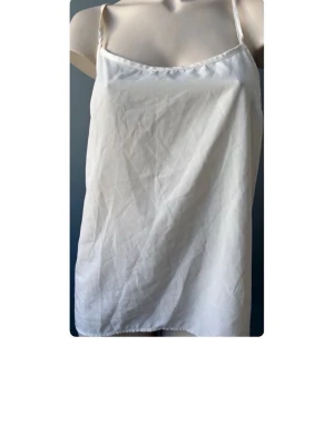 Beige linnetopp med korsade band - Stilren beige linnetopp med tunna axelband som korsas i ryggen. Toppen har en enkel och rak passform, perfekt för varma dagar. Materialet känns lätt och svalt, vilket gör den skön att bära. Snygg att matcha med jeans eller kjol.