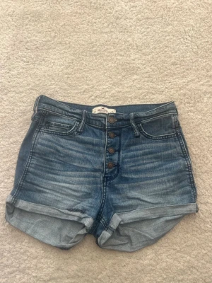 Blå jeansshorts, Hollister - Snygga blå jeansshorts från Hollister. fickor både fram och bak samt synliga knappar framtill. Storlek ”W 25”