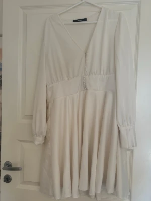 Vit omlottklänning från bik bok - Superfin vit kortklänning från Gina Tricot med v-ringning, långa ärmar och knappar framtill. Klänningen har en omlottliknande överdel och lätt utsvängd kjol. Perfekt för sommarens alla tillfällen!