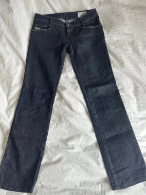 Mörkblå bootcut jeans från Diesel - Snygga mörkblå bootcut jeans från Diesel med klassisk femficksdesign och kontrastsömmar. Jeansen har låg midja och är tillverkade i ett slitstarkt denimtyg. Perfekta för dig som gillar en tidlös och cool look. Säljer då de är för stora på mig . Är öppen för pris förslag! 
