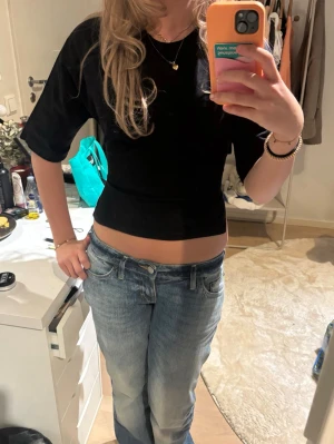 Svart croppad topp med knyt i ryggen - Trendig svart croppad topp med korta ärmar och snygg knytning i ryggen. Perfekt för dig som gillar en stilren men edgy look. Toppen har en tight passform och är tillverkad i ett mjukt material som känns skönt mot huden. 