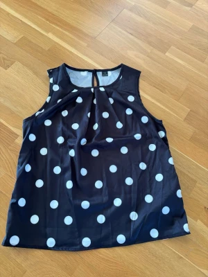 Prickig blus  - Snygg och klassisk blus med vita prickar.  Ärmlös blus med fin detalj vid halsen. Lätt och skönt material.