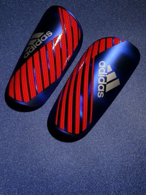 Adidas benskydd blå/röd - Snygga benskydd från Adidas i blått med röda diagonala ränder och vit logga. Perfekta för fotbollsträning eller match. Lätta och smidiga med en formad passform som ger bra skydd utan att vara i vägen.