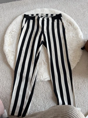 Randiga byxor från edc, svart/vit - Säljer ett par raka byxor från edc med svartvita vertikala ränder. Byxorna har normal midja och stängs med dragkedja och hake. Materialet känns mjukt och lätt, perfekt för en trendig look. Storlek 36 regular.