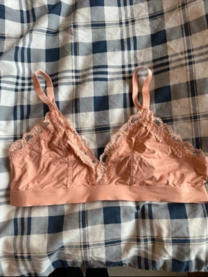 Rosa spetsbralette med smala axelband - Söt bralette i ljusrosa med spetsdetaljer längs kanterna och smala justerbara axelband. Mjuk och bekväm modell utan bygel, perfekt för en avslappnad stil. Materialet är tunt och stretchigt för extra komfort.