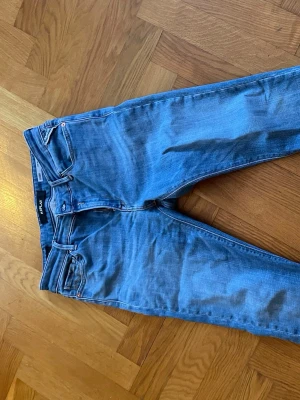 Blå skinny jeans från Nudie Jeans - Säljer ett par klassiska blå skinny jeans från Nudie Jeans. Modellen har fem fickor, dragkedjegylf och subtila slitningar för en avslappnad look. Tillverkade i mjuk denim med stretch för extra komfort. Perfekta till en casual outfit.