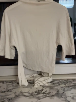 Vit knyt topp från Gina Tricot - Säljer en vit croppad topp från Gina Tricot i mjuk bomull. Toppen har korta ärmar och knytband i midjan som ger en snygg detalj. Perfekt till jeans eller kjol för en clean och fräsch look.