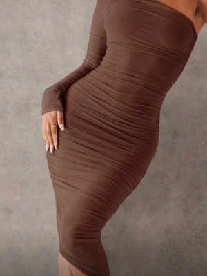 Brun one shoulder klänning - Snygg brun figurnära klänning med one shoulder-design och lång ärm på ena sidan. Klänningen har rynkade detaljer längs hela kroppen och är tillverkad i ett stretchigt material som framhäver siluetten. Perfekt för dig som vill sticka ut med en modern och trendig look.