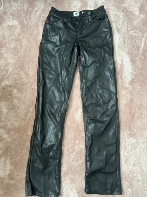 Svarta skinnbyxor från 157 - Snygga svarta skinnbyxor från 157 med klassisk femficksmodell och raka ben. Byxorna har bälteshällor, knapp- och dragkedjestängning samt silverfärgade nitar. 