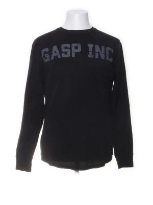 Svart långärmad tröja GASP INC - Svart långärmad tröja från GASP INC med tryckt logga över bröstet och en mindre logga i nacken. Tröjan har rund halsringning och är gjord i ett mjukt material som passar perfekt till träning eller till vardags