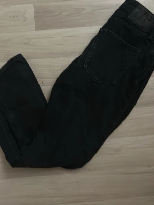 Svarta raka jeans - Säljer ett par svarta jeans med rak passform. Klassisk femficksmodell och knappgylf. Jeansen har en enkel och stilren look som passar till det mesta. Storlek 28/30 enligt etiketten. Perfekta för dig som gillar en clean och tidlös stil.