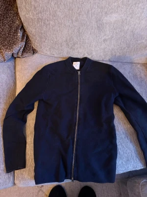 Mörkblå ziptröja  - Säljer en stilren mörkblå ziptröja från UNIQLO. Tröjan har hel dragkedja framtill, rund halsringning och långa ärmar. Perfekt att slänga på sig över en t-shirt för en enkel och clean look.