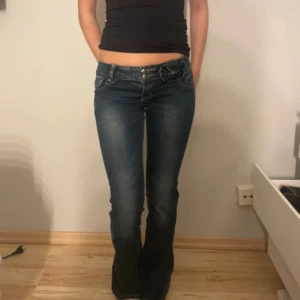 Mörkblå bootcut jeans med kontrastsömmar - As snygga jeans med rosett detalj! Den är utsydda hemma! Vet ej exat storlek men typ Xs/S hon på bilden är 166cm, mått finns på sista bilden!