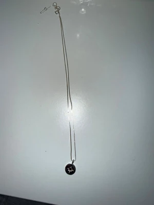 Silverhalsband med stjärnhänge - Snyggt halsband i silver med ett runt hänge som har en ingraverad stjärna och en liten röd sten i mitten. Kedjan är tunn och smidig, perfekt för att ge en stilren touch till din outfit. Passar dig som gillar enkla men unika smycken.