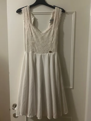 Vit spetsklänning med v-ringning Chiara Forthi Milano - Söt vit klänning med spets upptill och v-ringad hals. Kjolen är utsvängd och faller fint i kort längd. Klänningen har breda axelband och dragkedja i ryggen. Perfekt för sommarens alla tillfällen. Använd 2 ggr på student och skolavslutning, sista bilden ser man en svag missfärgning, antagligen av smink men inget man tänker på.