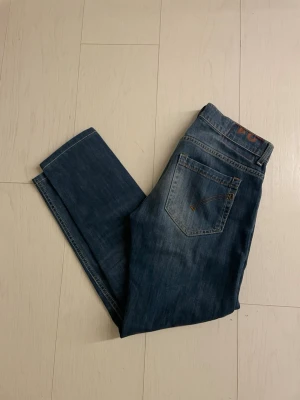 Dondups - Säljer ett par klassiska blå jeans från dondup med raka ben och femficksmodell. Jeansen har snygga slitningar och kontrastsömmar, 