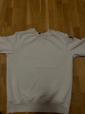 Vit sweatshirt från parajumpers  - Säljer en stilren vit sweatshirt från parajumpers med rund halsringning och ribbade muddar. Tröjan har diskreta röda sömmar på axlarna och en patch med logga på ena ärmen. Perfekt för en clean och avslappnad look. Den passar S också 