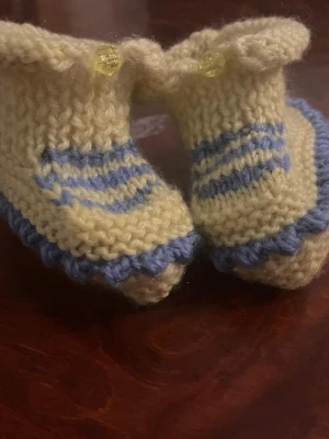 Stickade babystrumpor med blå detaljer - Supersöta ny  handstickade babystrumpor i ljusgult med blå ränder och blå kant. Strumporna har en liten volang upptill och dekoreras med en gul knapp. Perfekta för att hålla små fötter varma och mysiga.