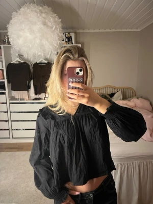 Svart blus med vidd - Trendig svart blus med lös passform. Blusen har långa, något puffiga ärmar med resår vid ärmslut och en slät struktur i tyget. Perfekt att styla med jeans för en cool look.