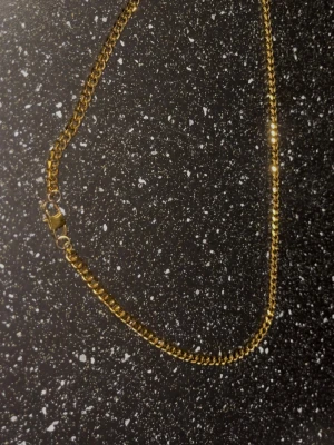 Kedjehalsband  i guldtonad metall - Snyggt halsband  i guldtonad metall med klassisk kedjedesign. Halsbandet har en robust karbinhake som lås och passar perfekt för dig som gillar stilrena accessoarer med lite edge. Levereras i en svart ask.