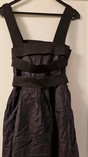 Svart klänning med breda band, Filippa K storlek S - Svart klänning med breda svarta band i midjan och över bysten. Klänningen har en voluminös kjol. Perfekt för dig som vill sticka ut med en cool och edgy stil. Storleken är i S inom dam och är från Filippa K.