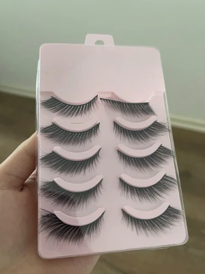 Svarta volymfransar i 5-pack - Säljer ett set med fem par svarta lösögonfransar med volym och fluffig design. Fransarna har en naturlig böj och sitter på en tunn, flexibel remsa. Perfekta för att framhäva ögonen och skapa en dramatisk look.