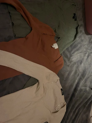 3 ribbstickade tröjor från amisu, h&m och gina - Tre ribbstickade långärmade tröjor från Amisu i färgerna grön, rostbrun och beige. Alla har rund halsringning och är tillverkade i ett mjukt, stretchigt material som sitter snyggt på kroppen. Perfekta basplagg för lager-på-lager-stil.