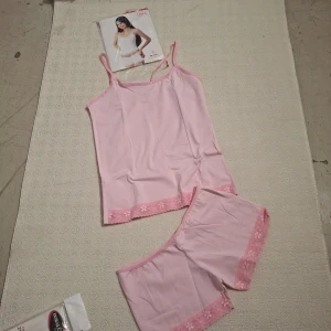 Ljusrosa pyjamasshorts med spetskant - Säljer ett par ljusrosa pyjamasshorts från Cansoy med söt blommig spetskant nertill. Shortsen har en loose passform och är gjorda i mjuk bomull, perfekta för sommarnätter. Matchande linne med smala axelband ingår.