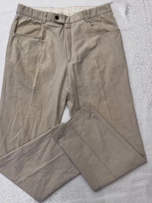 Beige linnebyxor från balmain med raka ben - Snygga beige linnebyxor med raka ben och klassisk passform. Byxorna har framfickor, bälteshällor och stängs med knapp och dragkedja. Perfekta för en avslappnad och stilren look. Materialet är lätt och luftigt linne. Liten fläck på benet se bilder🚨