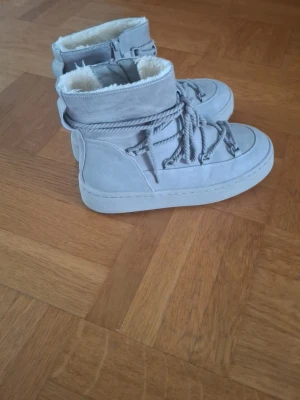 Gråa fodrade kängor med snörning - Säljer ett par gråa kängor med grov snörning och dragkedja på sidan. Insidan är fodrad med mjuk, beige fuskpäls som gör dem extra sköna och varma. Yttermaterialet är mockaliknande och sulan är i matchande grå ton. Perfekta för kalla dagar. 