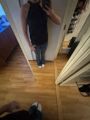 Svart halterneck topp - Snygg svart halterneck topp med hög hals och ärmlös design. Perfekt att matcha med jeans eller kjol för en trendig look. Toppens material känns mjukt och följsamt mot kroppen.