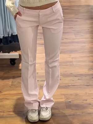 Ljusrosa kostymbyxor - Säljer ett par ljusrosa kostymbyxor med låg midja passform och pressveck. Byxorna har hällor för skärp och två fickor fram. Perfekta för en trendig och stilren look.