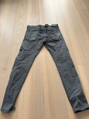 Gråa slim fit jeans från Replay - Snygga gråa slim fit jeans från Replay med klassisk femficksdesign och knappgylf. Jeansen har en något tvättad look och raka ben. Perfekta för dig som gillar en stilren och avslappnad vibe.