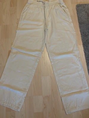 Beiga linnebyxor från RYVLS - Snygga och luftiga beiga linnebyxor från RYVLS med raka ben och resår i midjan. Perfekta för en avslappnad och stilren look. Byxorna har fickor på sidorna och är tillverkade i ett lätt och svalt linnematerial.