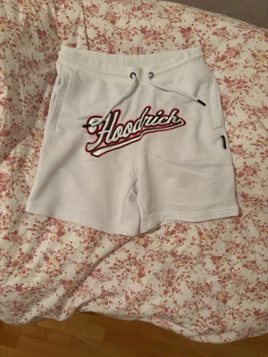 Vita Hoodrich shorts med snörning - Säljer ett par vita shorts från Hoodrich med broderad logga framtill och 'Hood Series' tryck bak. Shortsen har snörning i midjan, sidofickor och en bakficka. Perfekta för sommaren och riktigt sköna att bära! De är helt fläckfria dvs helt vita🤝‼️