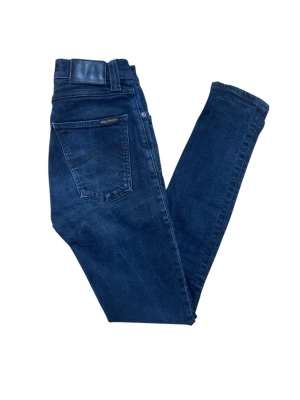 Mörkblå jeans från Nudie Jeans - Snygga mörkblå  jeans från Nudie Jeans med klassisk femficksdesign och diskret logga på bakfickan. Jeansen har hög midja och är tillverkade i mjukt bomullsmaterial med stretch för extra komfort.