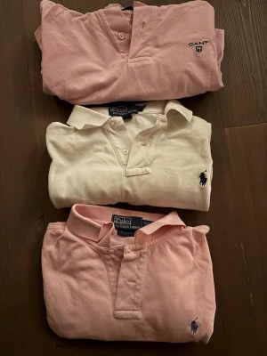 Pikétröjor från Gant och Polo Ralph Lauren - Tre klassiska pikétröjor, två i ljusrosa och en i vit, från Gant och Polo Ralph Lauren. Alla har krage, knappar framtill och broderad logga på bröstet. Perfekta för en stilren och avslappnad look. Ljus rosa peken är storlek L/ G , vita peken är storlek M och Gant peken är storlek L. ALLT säljes tillsammans för ett pris.