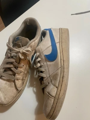 Nike vita sneakers med blå swoosh - Klassiska vita Nike sneakers med blå swoosh på sidan.  Väl använda och lite smutsiga, men har mer att ge.