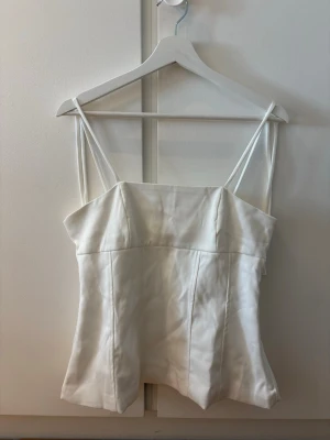 Vit korsettopp med smala axelband - Snygg vit korsettopp med smala axelband. Toppen har en lätt strukturerad passform och är perfekt för sommaren. Materialet känns mjukt och har en lätt glans. Säljer då den är för stor🤍