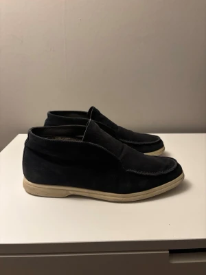 Mörkblå mocka loafers - Säljer ett par mörkblå loafers i mocka med vit sula. Skorna har en klassisk slip-on design och är fodrade med mjukt material på insidan för extra komfort. Perfekta för dig som gillar stilrena och bekväma skor.